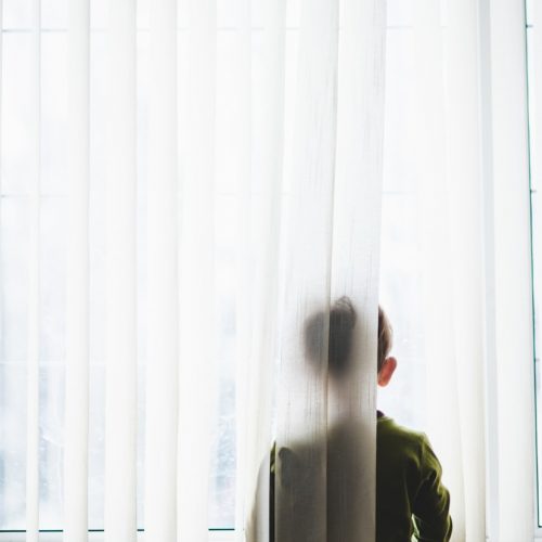 man in green coat standing near white window curtain